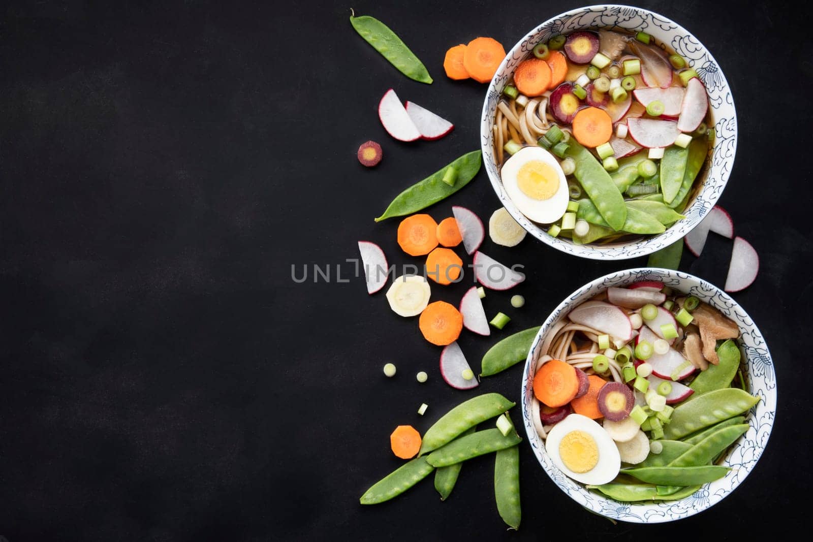 Two bowls of udon nooodle soup with fresh vegetables and hard boilled egg: flat lay with copy space.