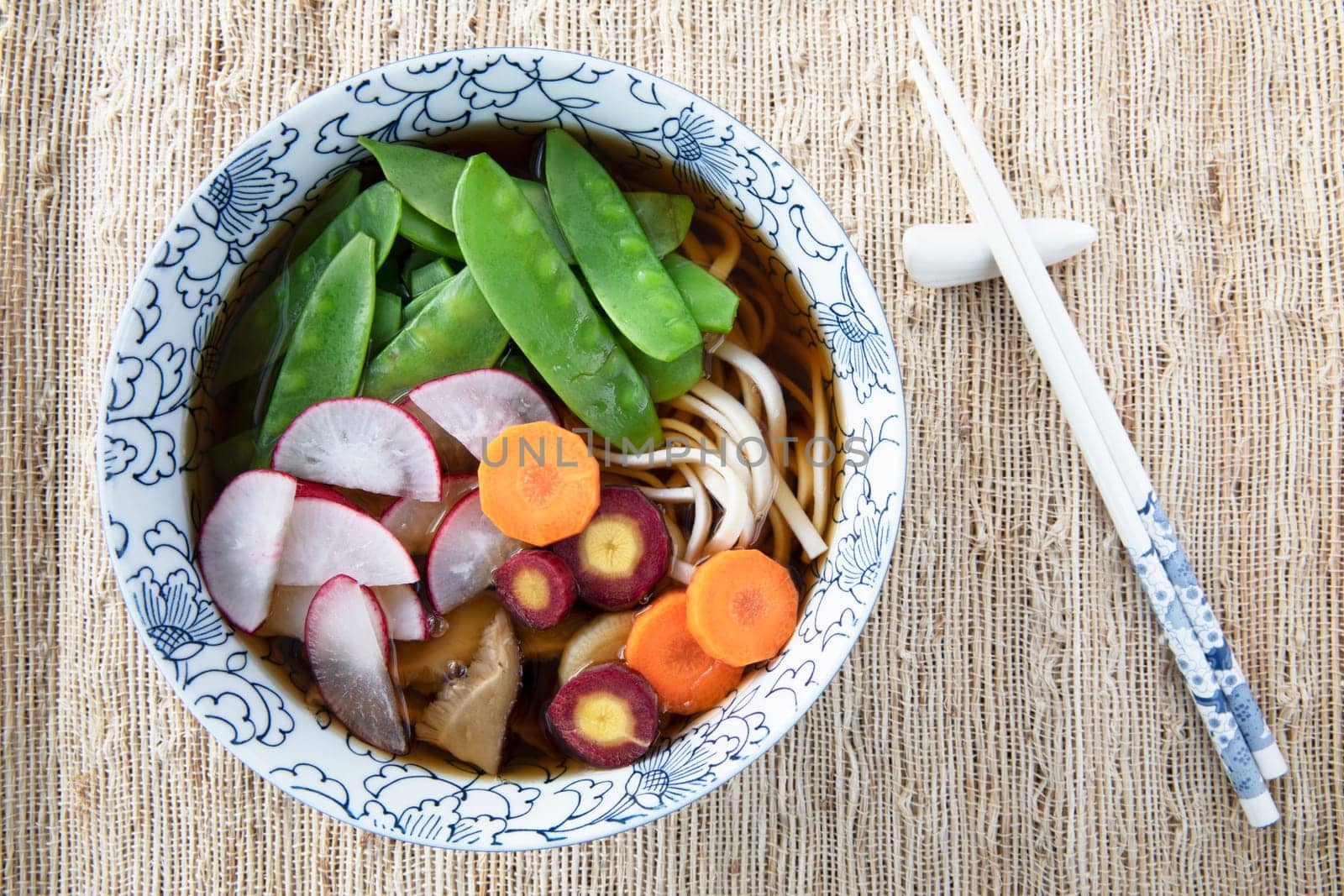 Filling bowl with udon noodle soup series image seven: bowl with noodles, shiitake mushrooms, snow peas, broth, radishes, and carrots