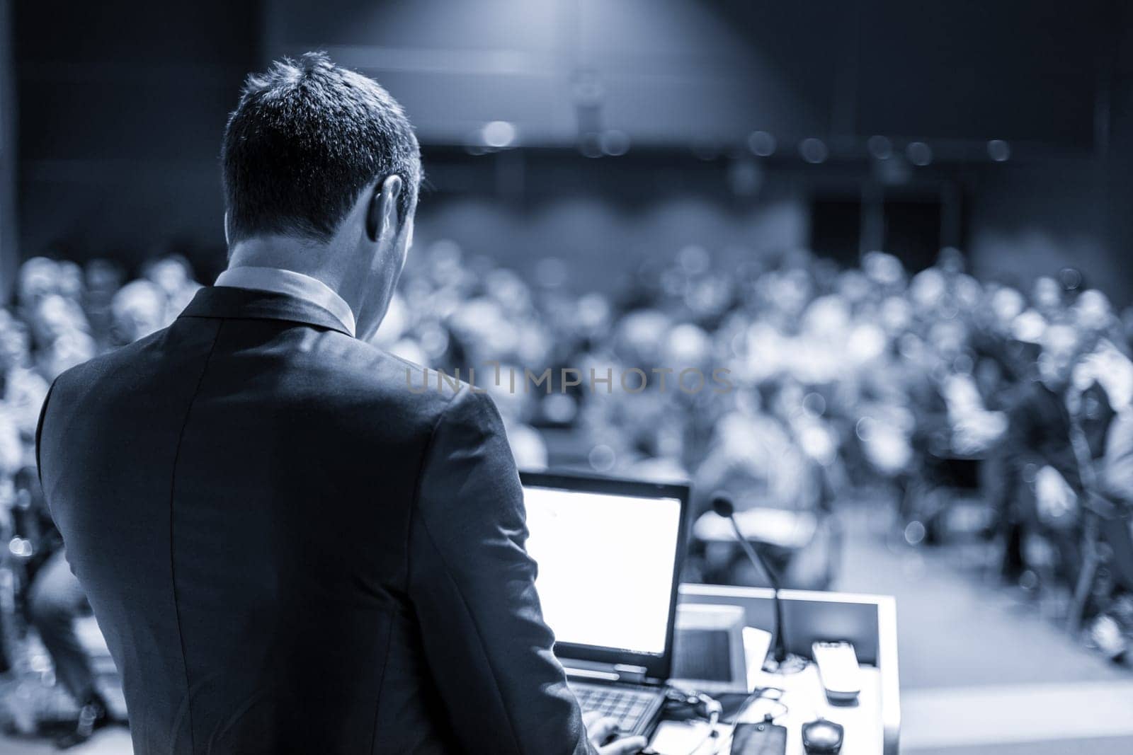 Speaker giving a talk on corporate business conference. Unrecognizable people in audience at conference hall. Business and Entrepreneurship event. Blue toned grayscale image.
