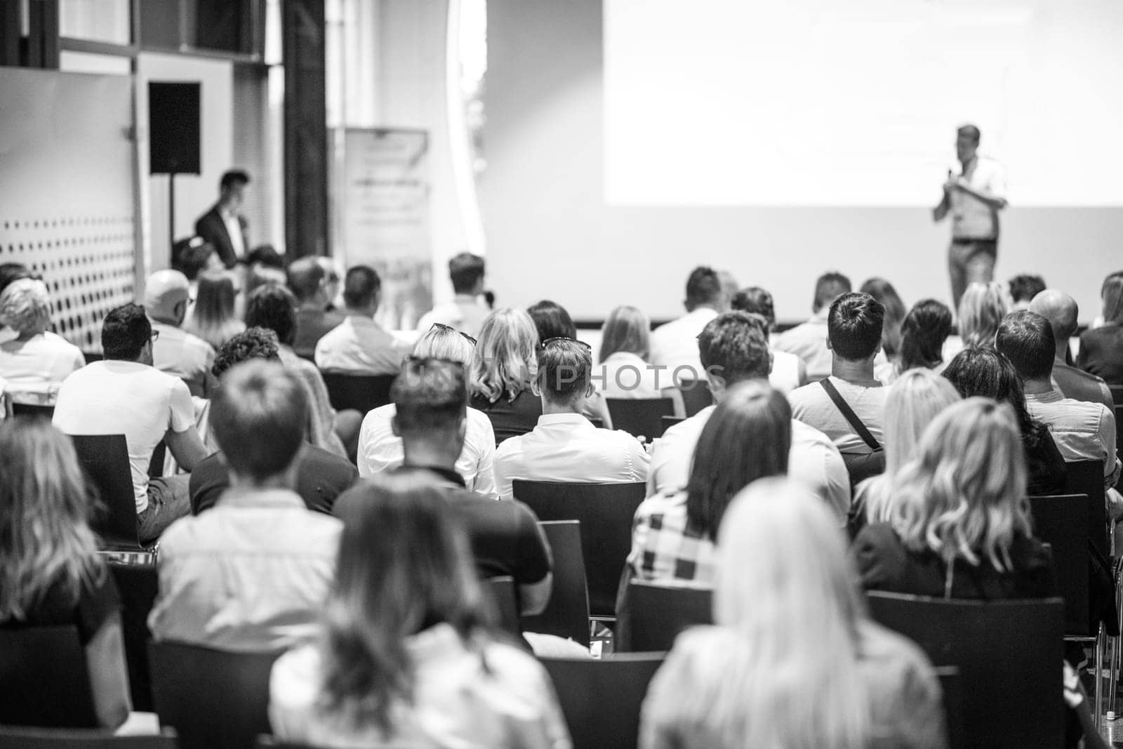 Speaker giving a talk in conference hall at business event. Focus on unrecognizable people in audience. Business and Entrepreneurship concept. Black and white image.
