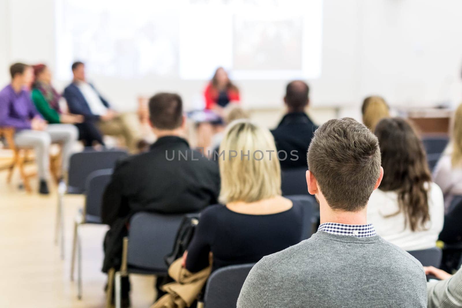 Female speaker giving presentation in lecture hall at university workshop. Audience in conference hall. Rear view of unrecognized participant in audience. Scientific conference event.