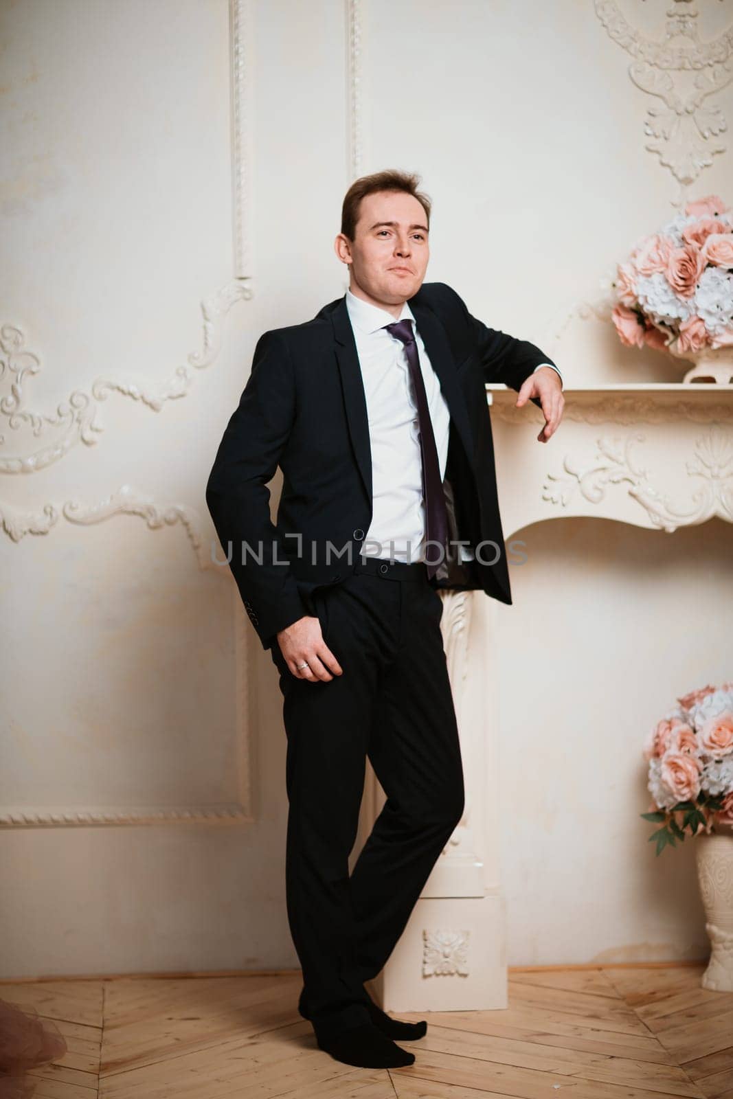 Portrait groom man in black suit on light background.