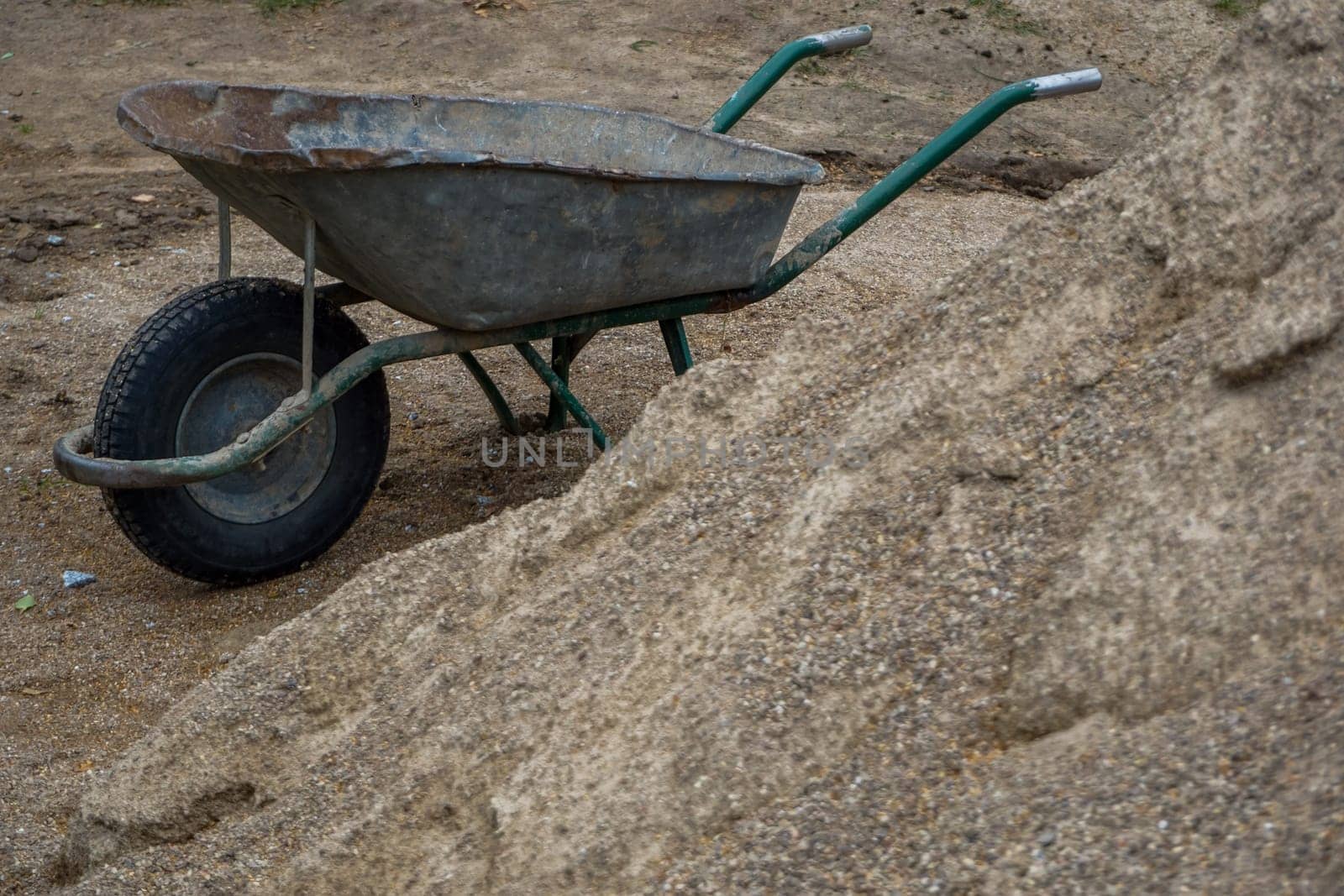 Construction wheelbarrow in the sand by the river Daugava. Wheelbarrow at the gravel pile, Latvia. Wheelbarrow for construction in site building area.