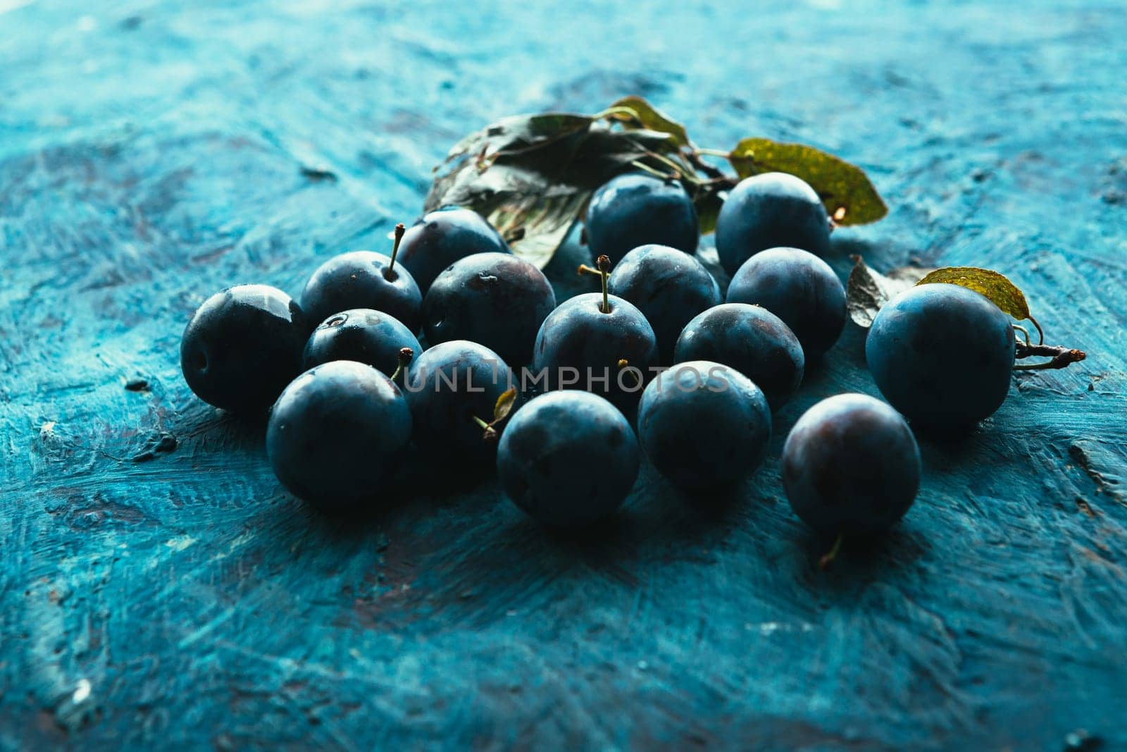 many fresh plums on blue background close up.