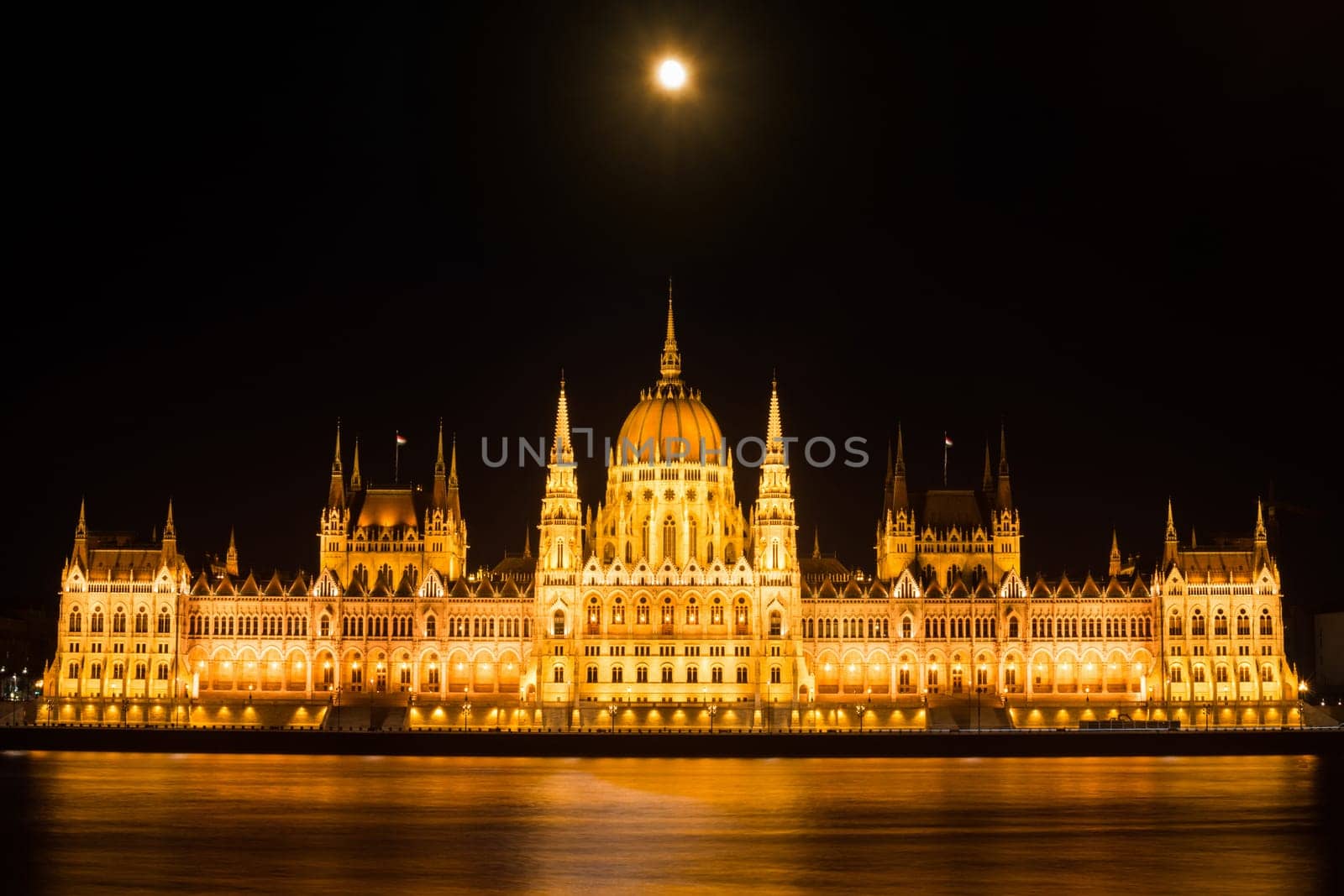 Landmark of Hungarian parliament building in Budapest at night with moon on dark black sky.