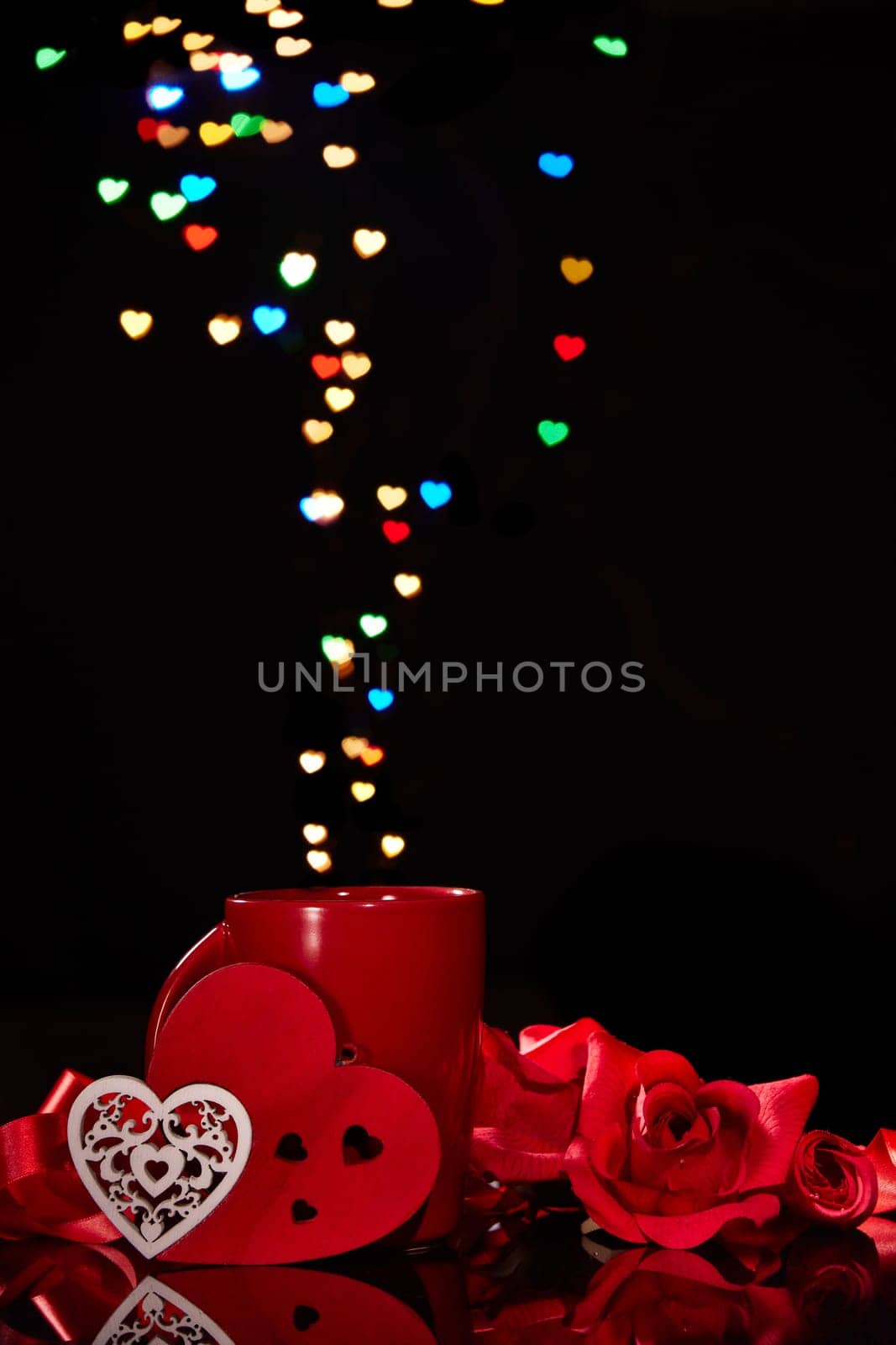 Still life: Cup of coffee, red heart and roses on black background with heart-shaped bokeh. Copy space. Valentine's Day setting table. Design element for romantic greeting card, festive menu of cafe