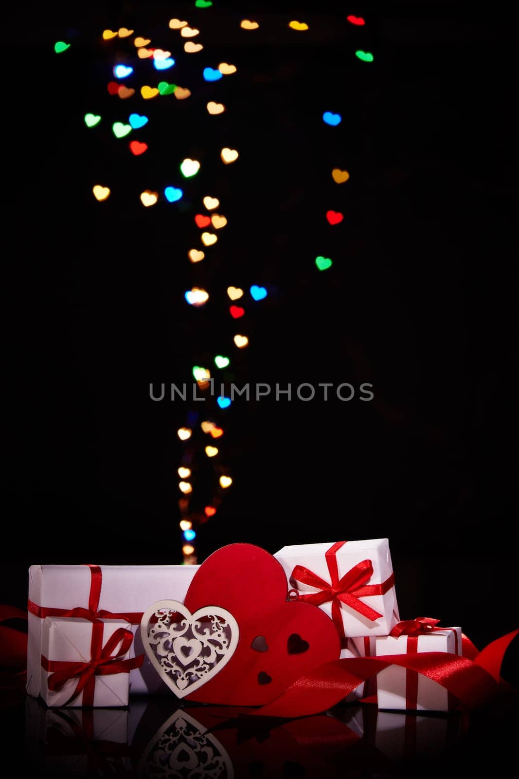 Gift boxes and red hearts on a black background with heart-shaped bokeh . Valentine's Day card with copy space. Design element for romantic greeting card, wedding invitation
