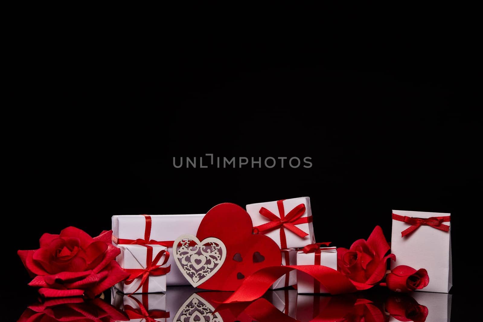 Gift boxes and red roses and decorative heart on black background. Valentine's Day card with copy space. Design element for romantic greeting card, wedding invitation
