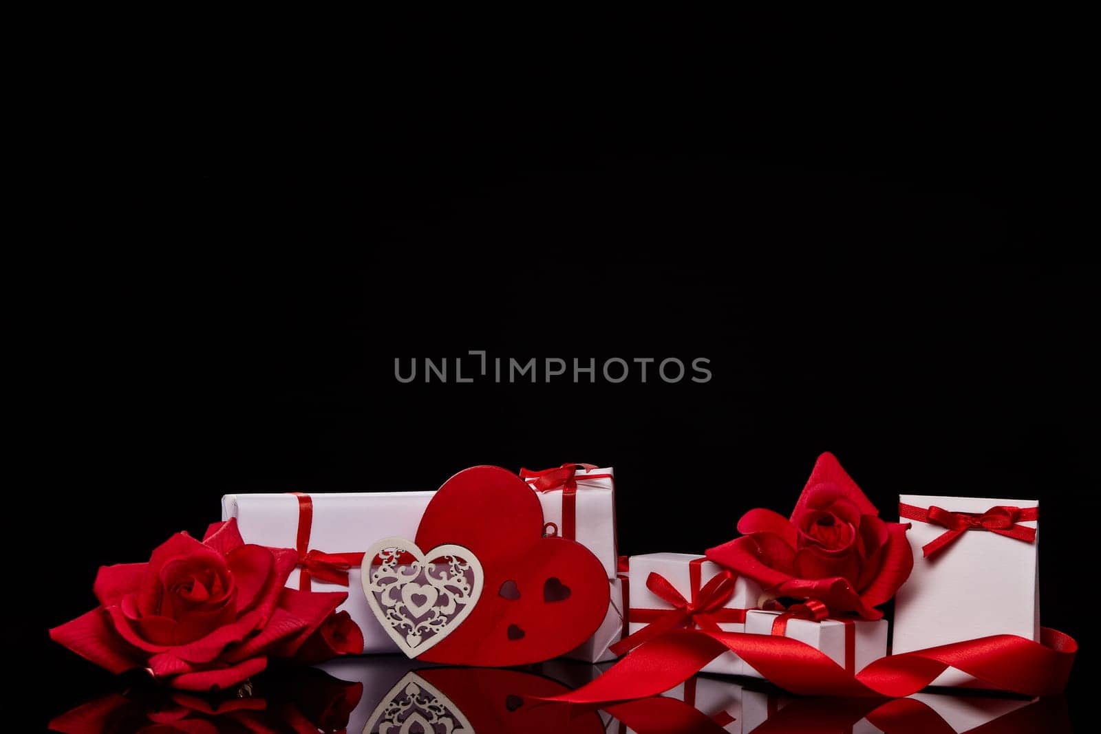 Gift boxes and red roses and decorative heart on black background. Valentine's Day card with copy space. Design element for romantic greeting card, wedding invitation