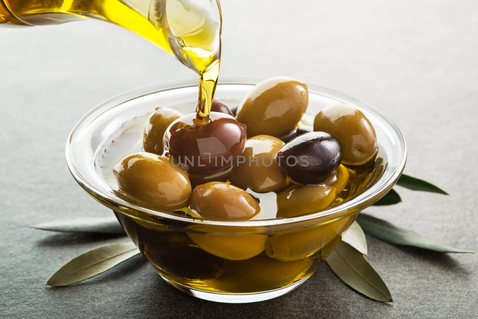 Organic olive oil. Bottle of Extra virgin oil pouring in to glass bowl with olives
