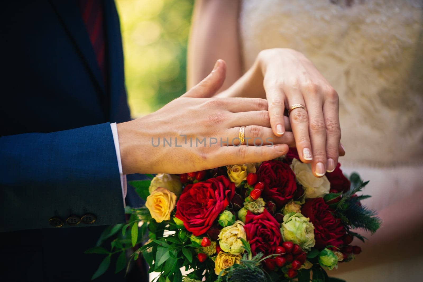hands of the bride and groom on a bouquet.