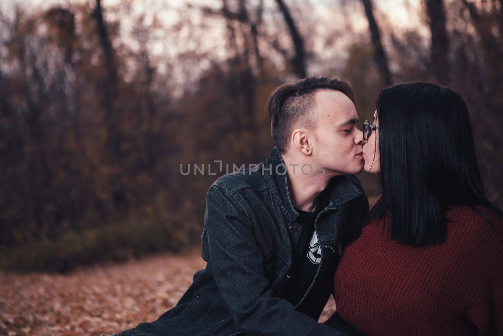 young man and young woman are sitting on a plaid in an autumn forest.
