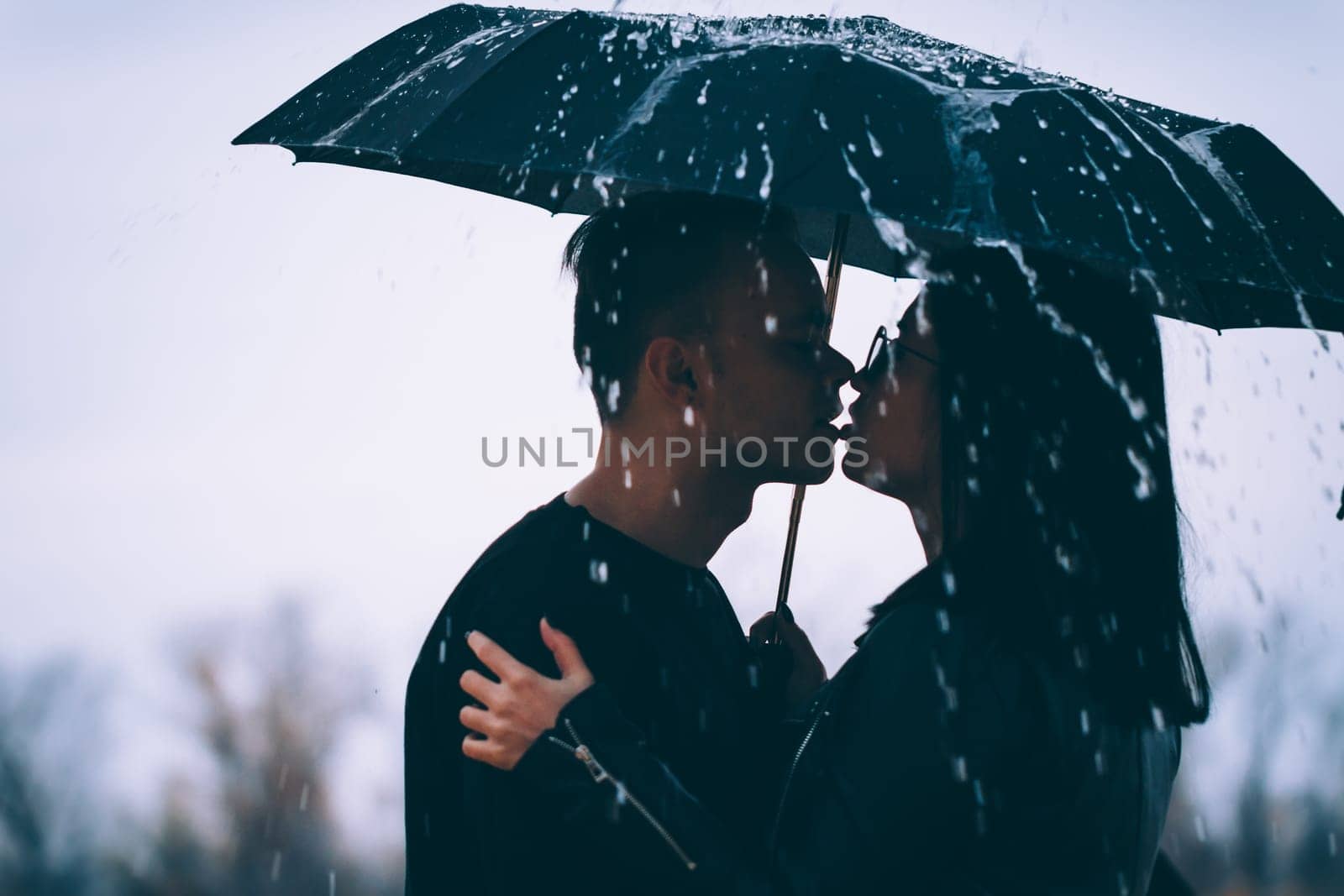 young couple standing under a dark umbrella.