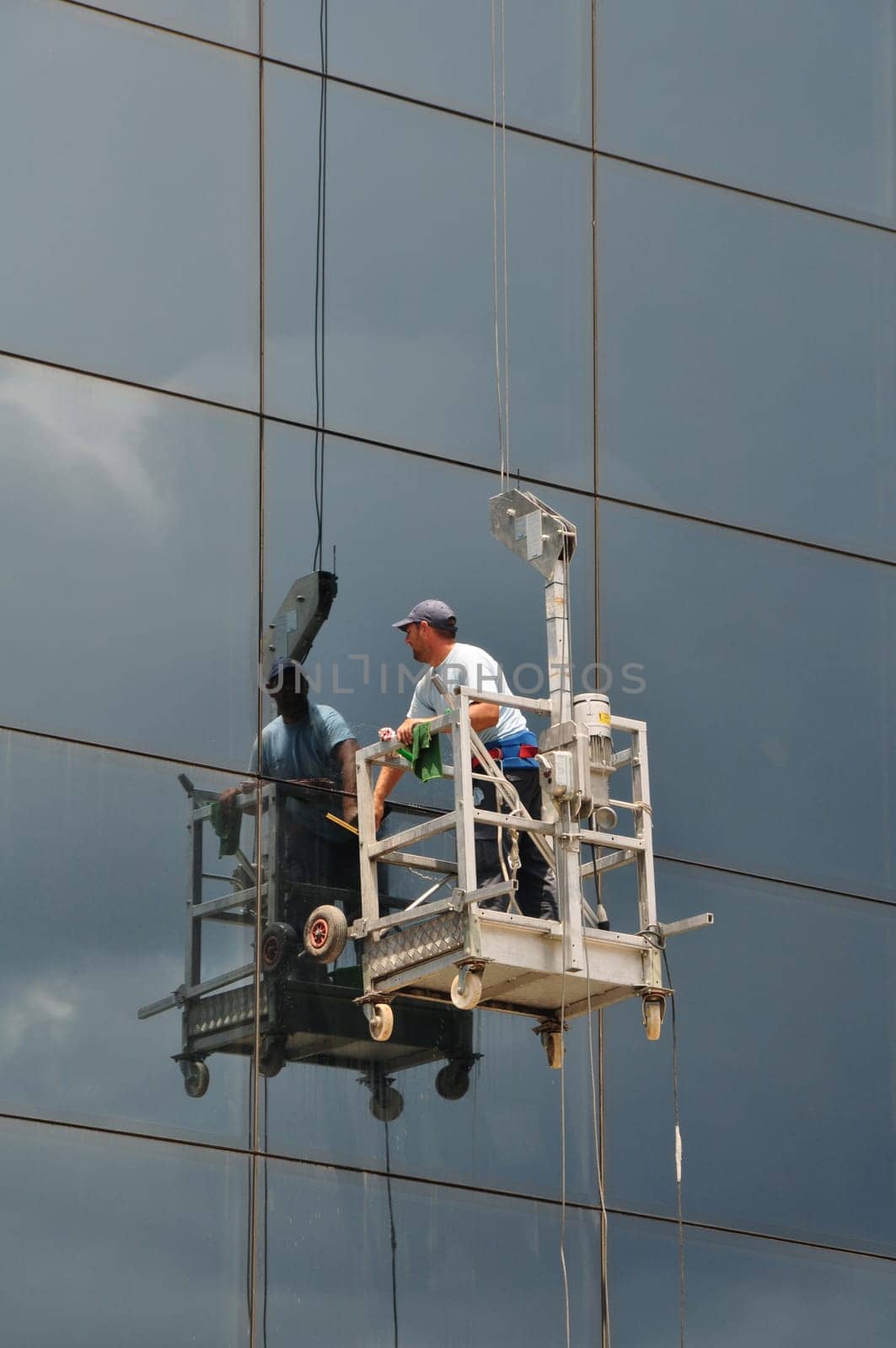 ATHENS, GREECE - JULY 24, 2014: Man cleaning the windows of high rise building glass facade. Working at height dangerous occupation.