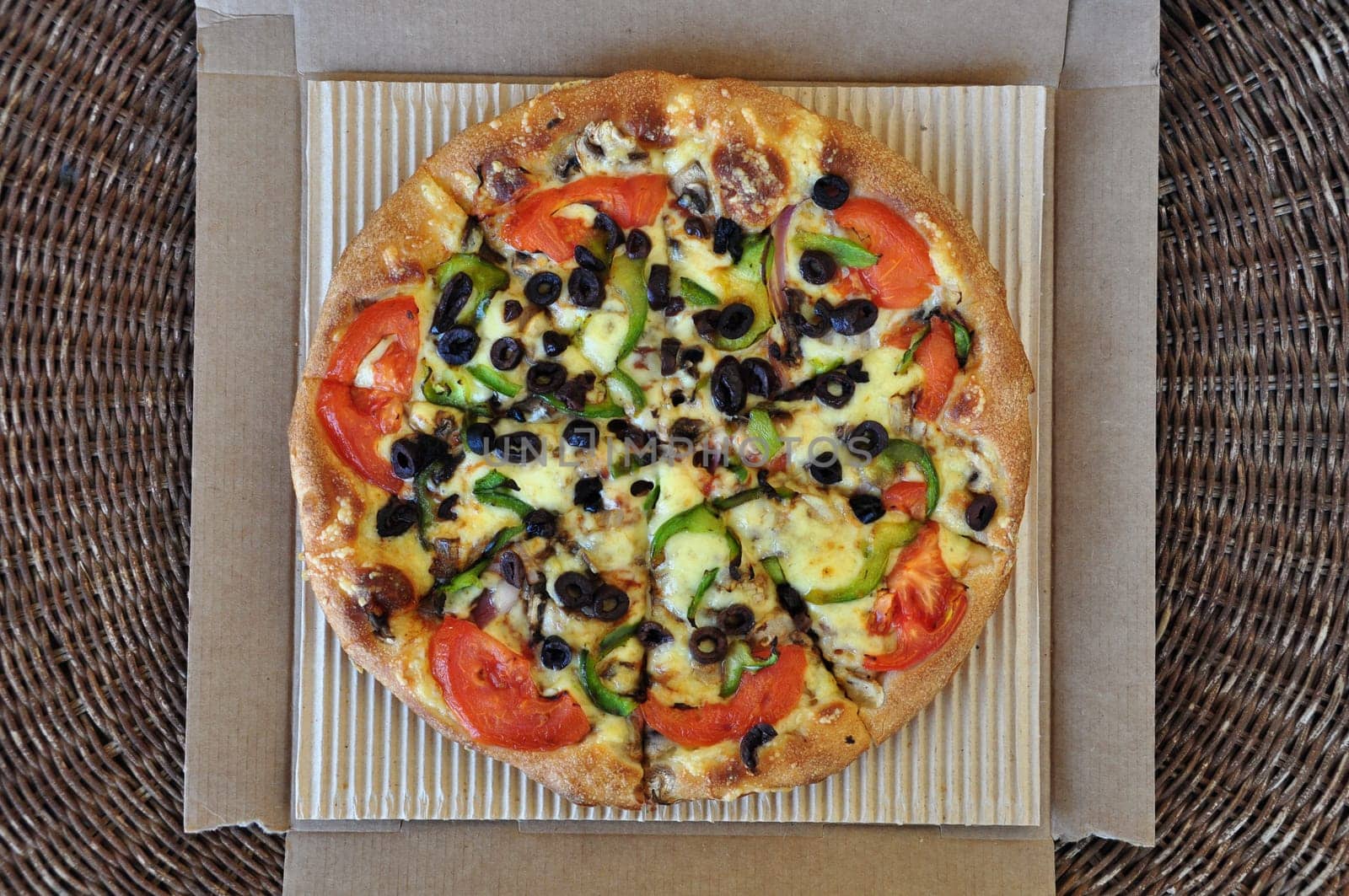 Vegetarian pizza with tomato, olives, pepper, mushrooms and onions packaged in cardboard box. Italian takeaway food background.