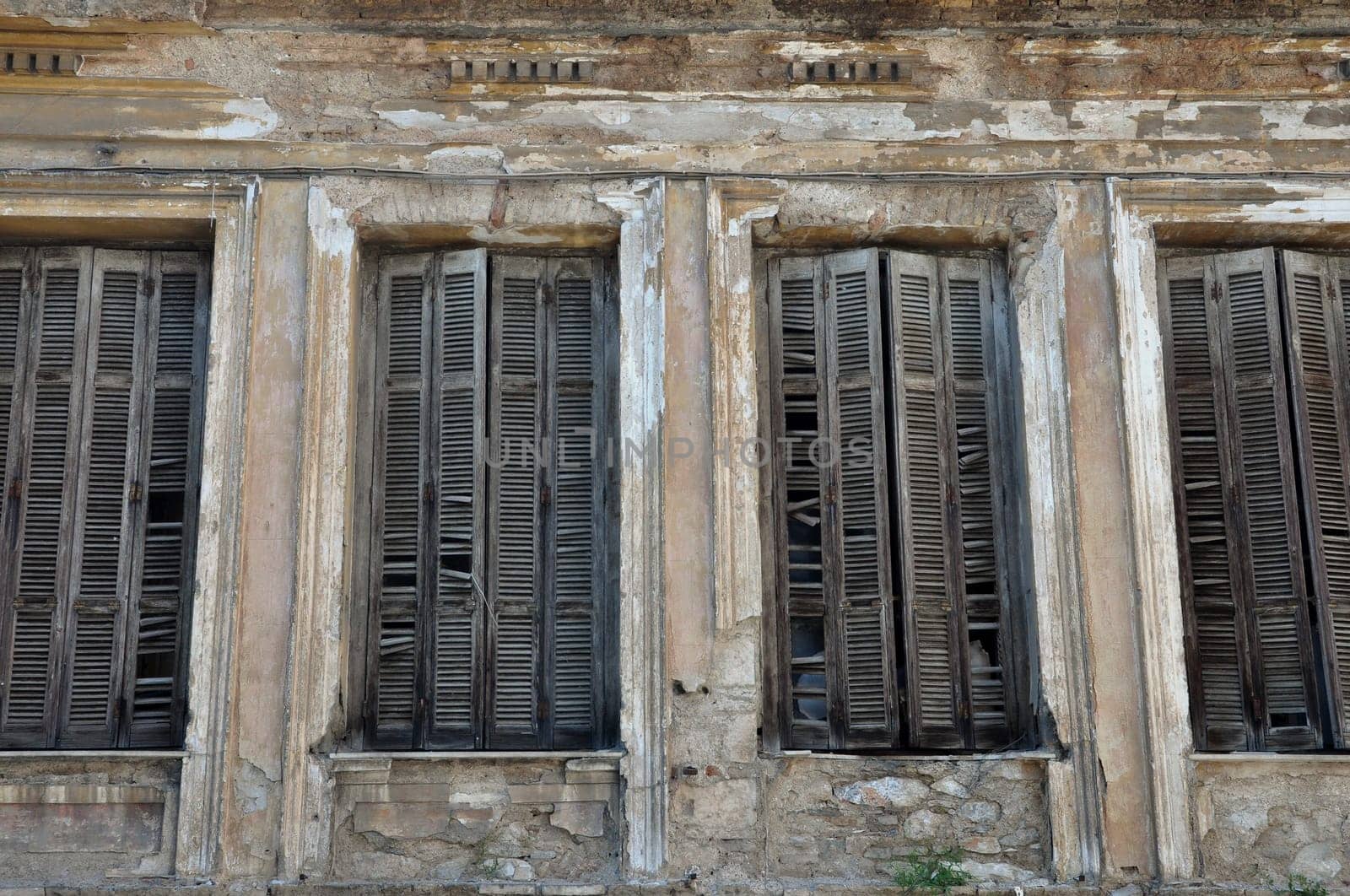 Broken wooden window shutters and chipped wall of a decayed building.
