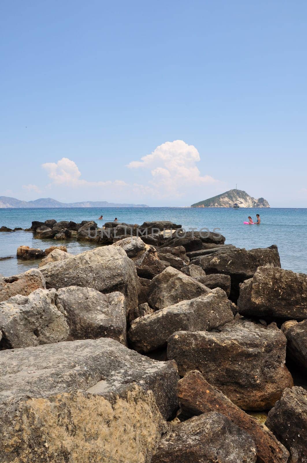 ZAKYNTHOS, GREECE - JULY 17, 2014: People swimming at the beach in Keri. Rock pier blue sea and sky horizon.
