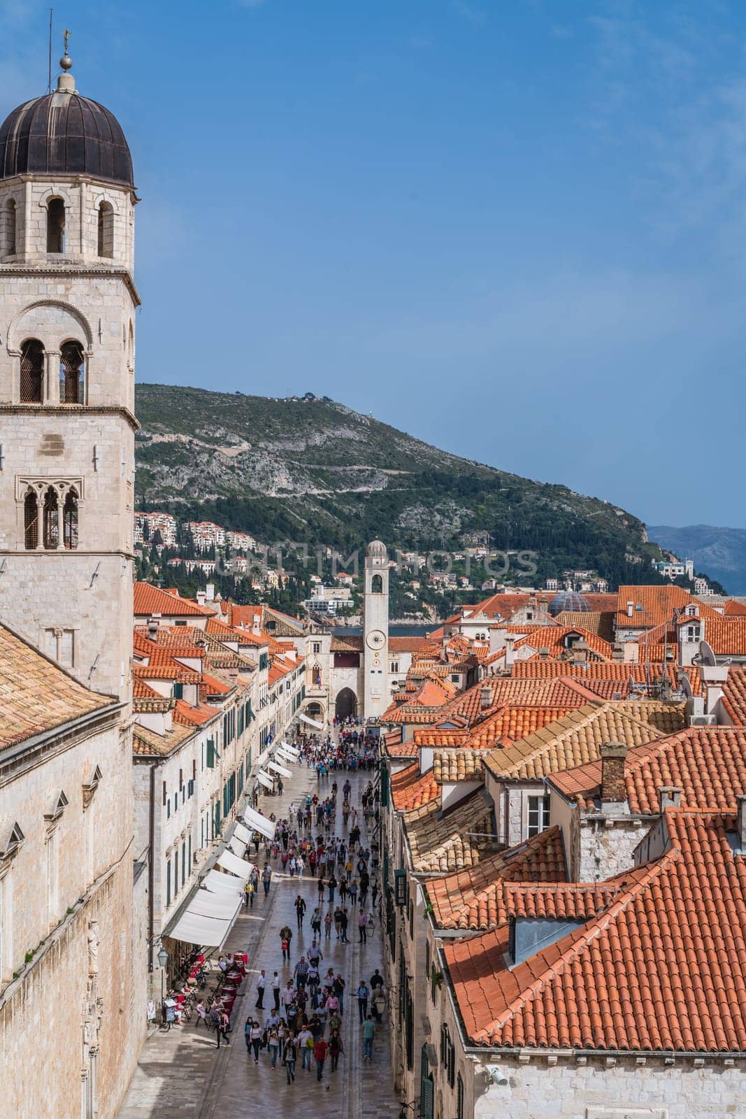 Dubrovnik, Croatia - April 2018 : Tourists walking on the main street below the church bell tower and rooftops of old houses in Dubrovnik, viewed from the Old Town fortified walls