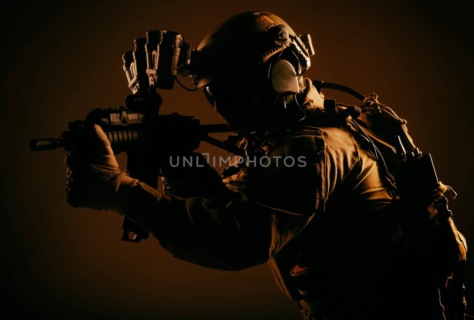 Army elite forces soldier, special security service fighter in tactical gear and ammunition, night vision device on helmet, aiming short barrel rifle, sneaking in darkness, low key with red backlight