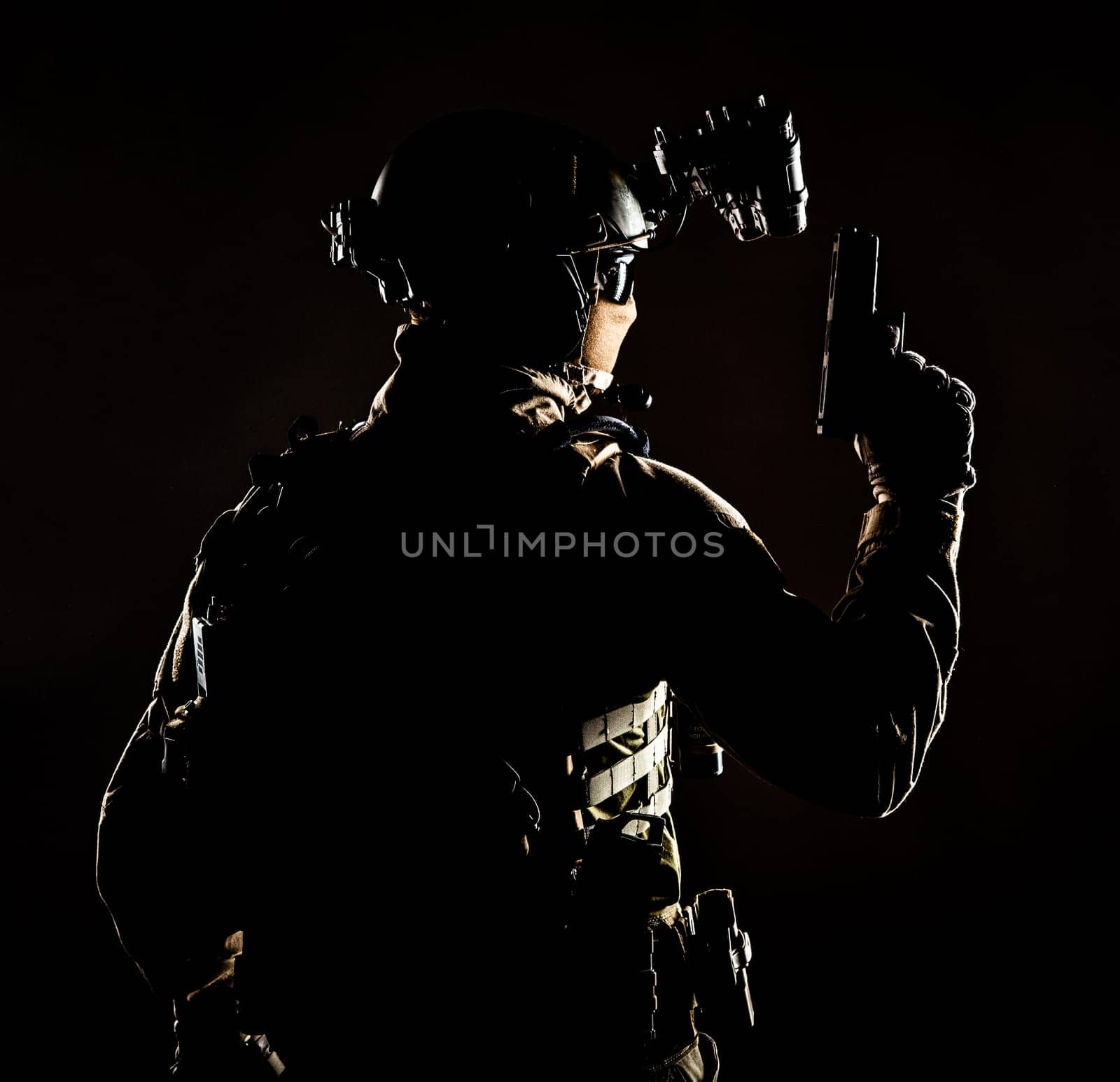 Army elite forces soldier, police special operation, counter terrorist team member in tactical ammunition with hidden behind mask identity, standing backwards with pistol in hand, low key studio shoot