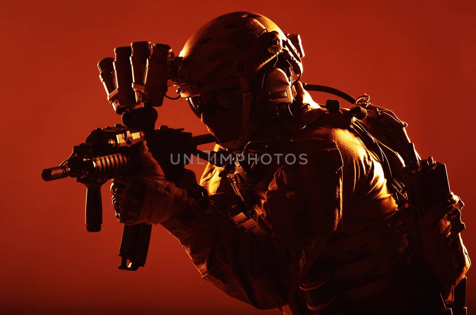 Army special operations soldier, commando fighter in full tactical ammunition, helmet with radio headset and night vision device, aiming short barrel assault rifle in darkness, low key studio shoot