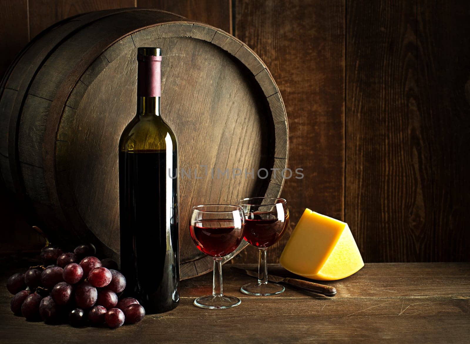 Bottle of red wine with glasses and cheese on wooden and barrel background.