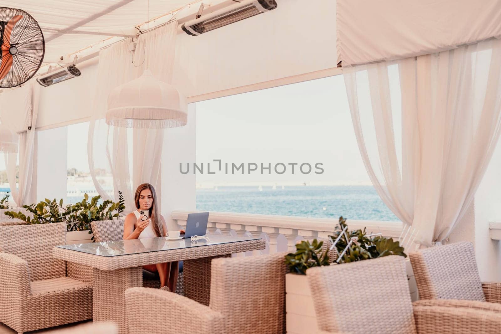 Woman coffee cafe laptop sea. Female freelancer using laptop on coffee break in modern cafe with sea view in the morning.