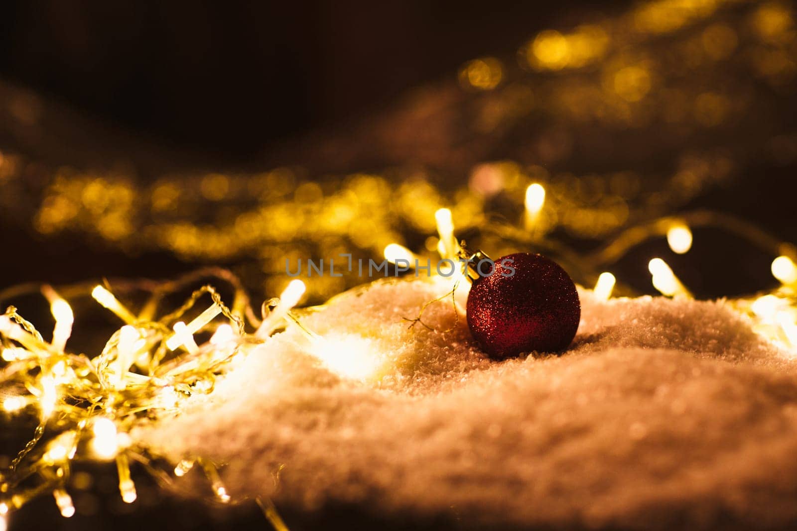 red Christmas ball and luminous garland on the snow.