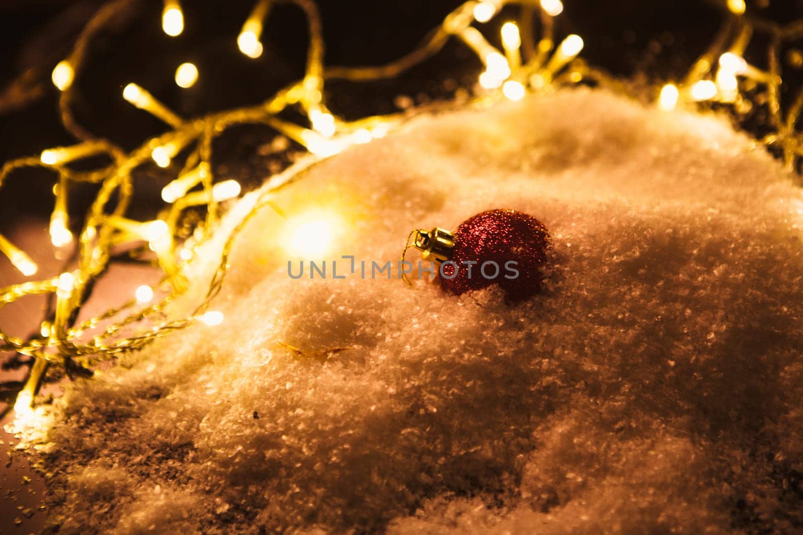 red Christmas ball and luminous garland on the snow.
