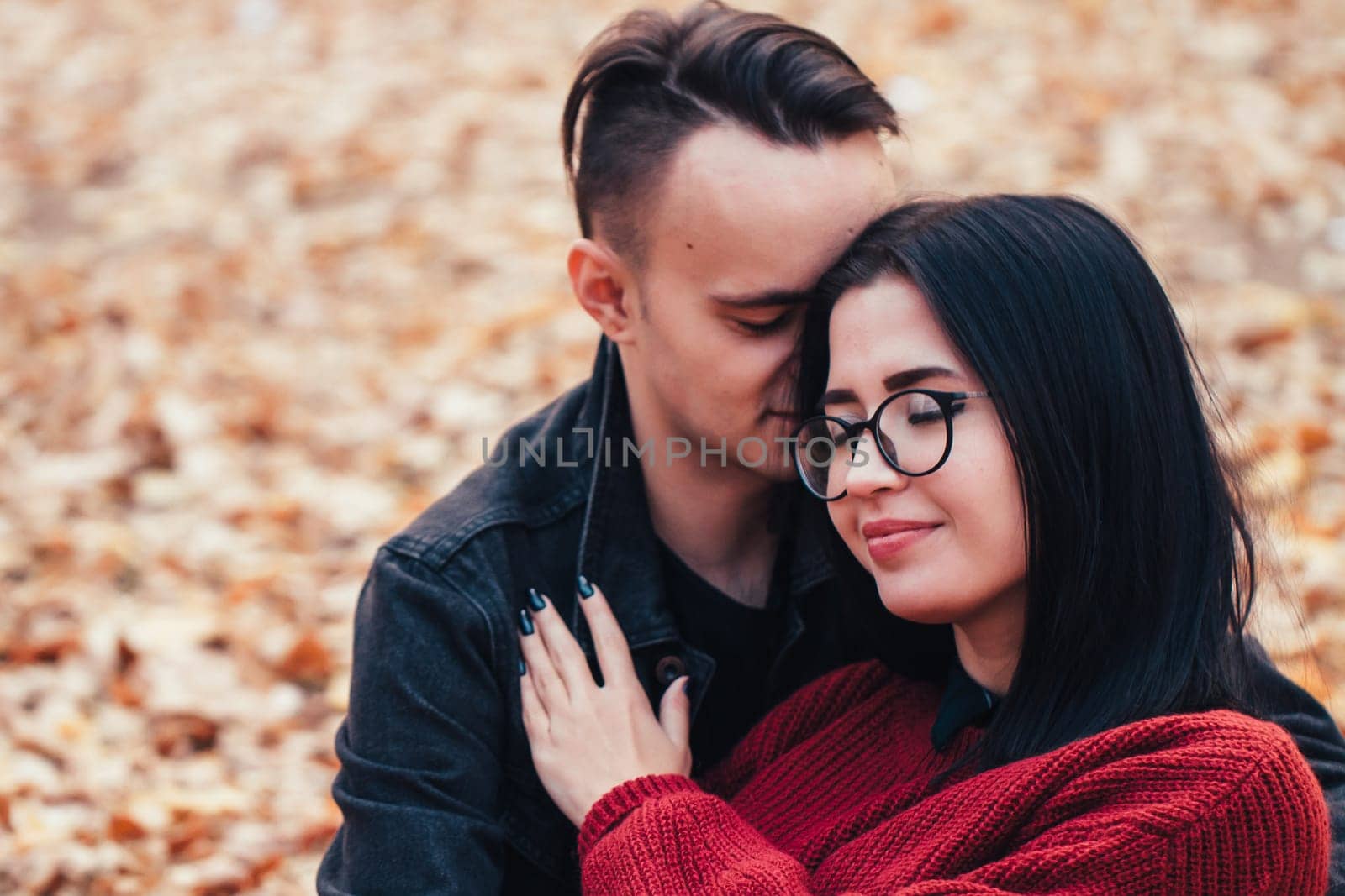 young man and young woman are sitting on a plaid in an autumn forest.