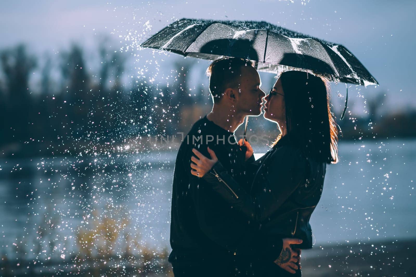 young couple standing under a dark umbrella.