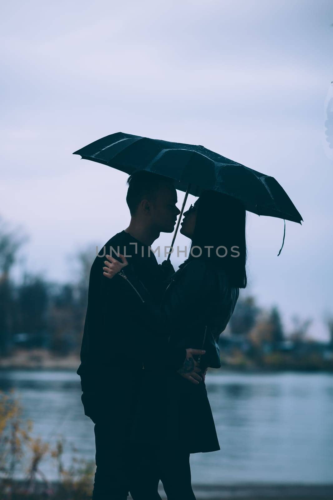 young couple standing under a dark umbrella.