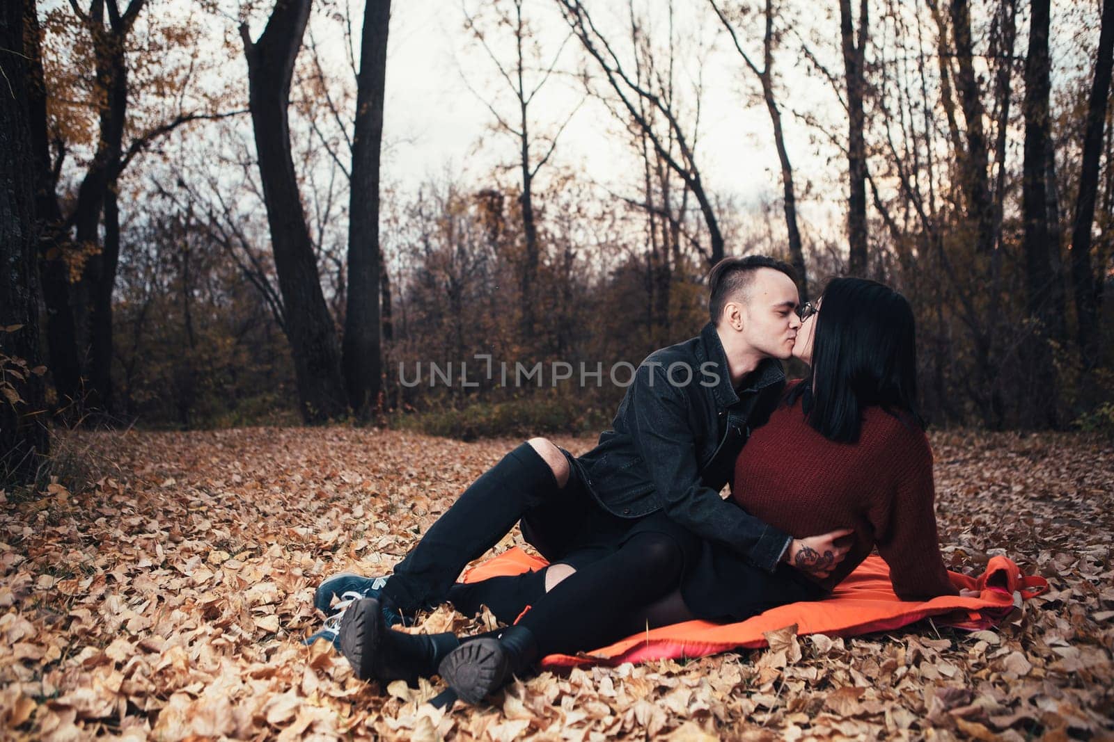 young man and young woman are sitting on a plaid in an autumn forest.