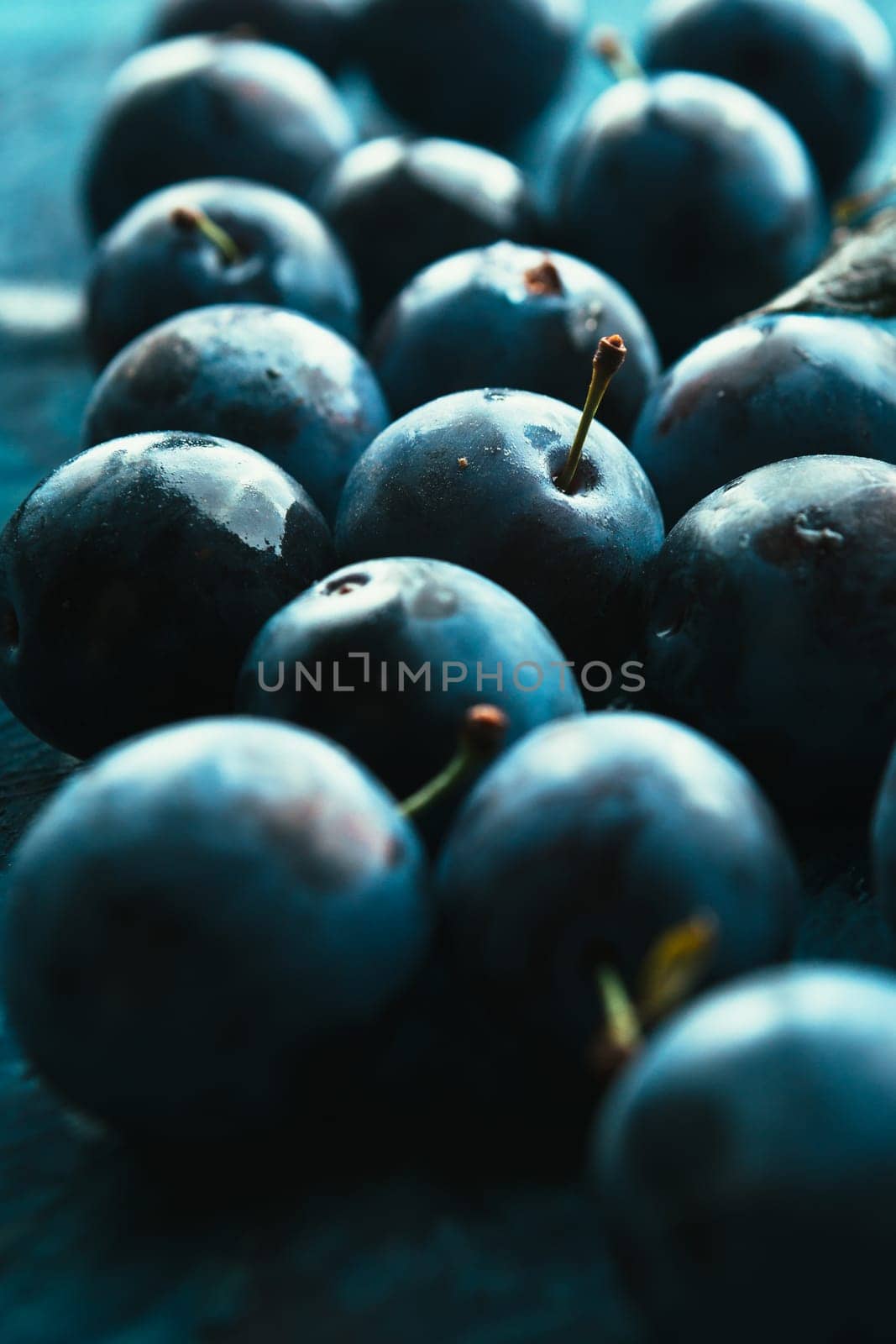 many fresh plums on blue background close up.