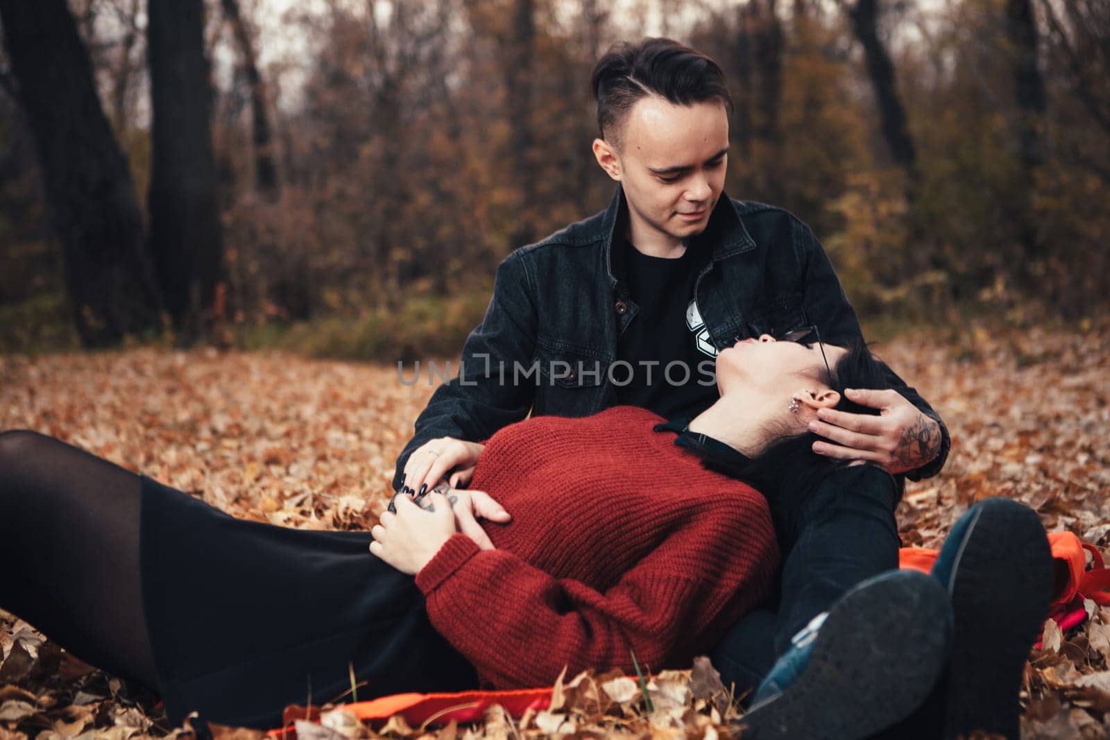 young man and young woman are sitting on a plaid in an autumn forest.