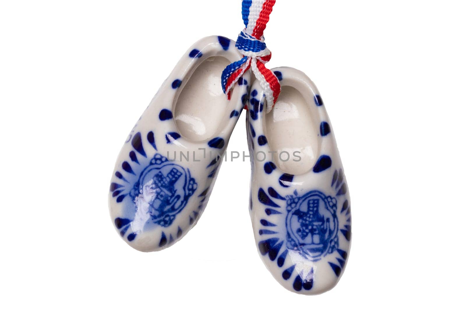 Holland wooden clogs. A pair of traditional dutch porcelain shoes with a ribbon flag isolated on a white background. Souvenir from Amsterdam. Macro.