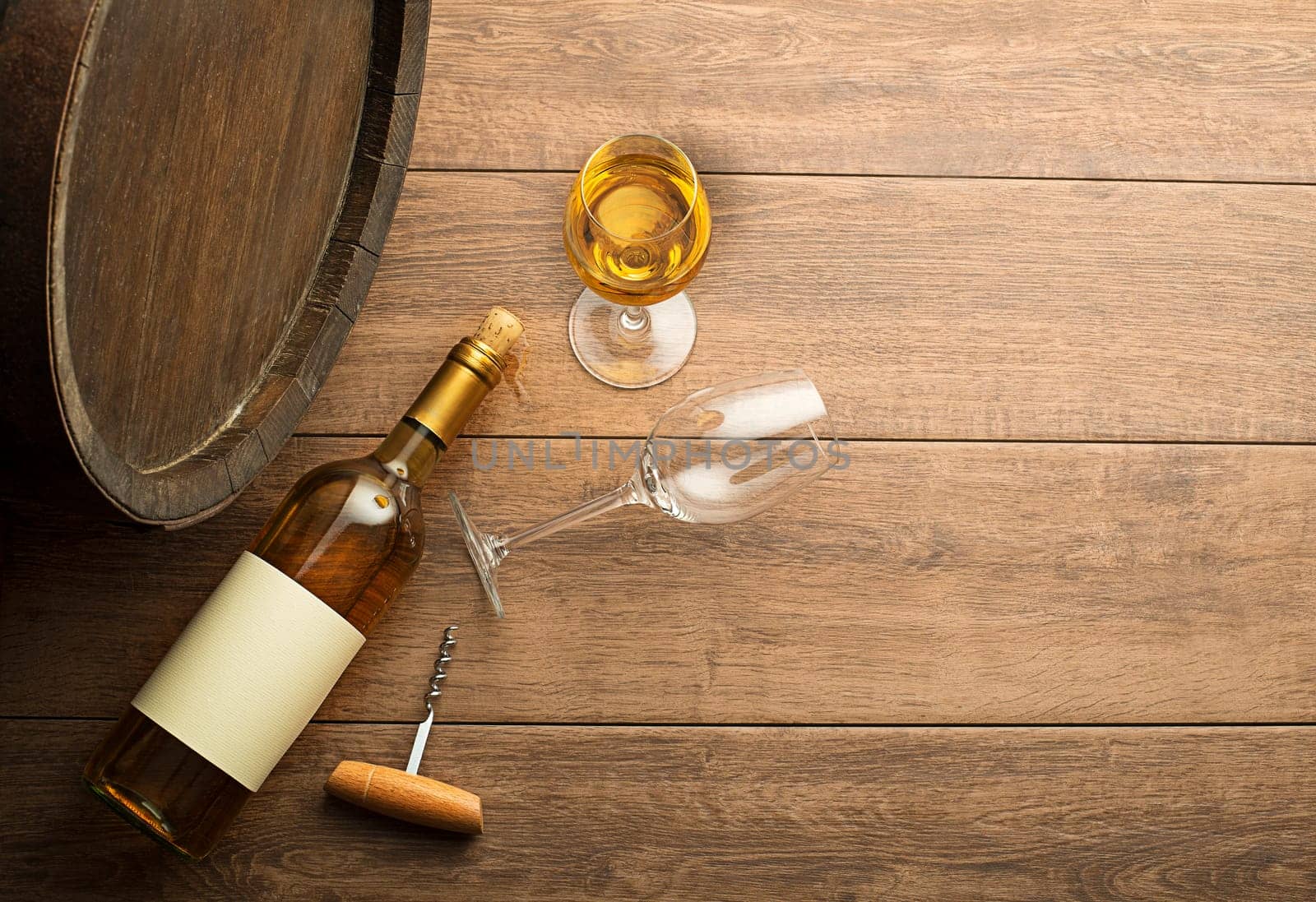 Bottle of white wine with label on old board. Wine bottle and glass with barrel background
