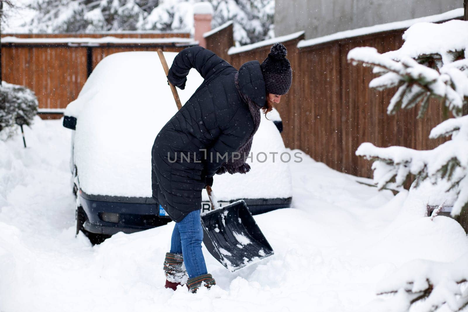woman with shovel cleaning snow aeound car. Winter shoveling. Removing snow after blizzard