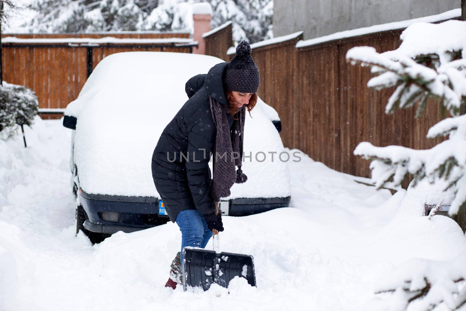 woman with shovel cleaning snow aeound car. Winter shoveling. Removing snow after blizzard