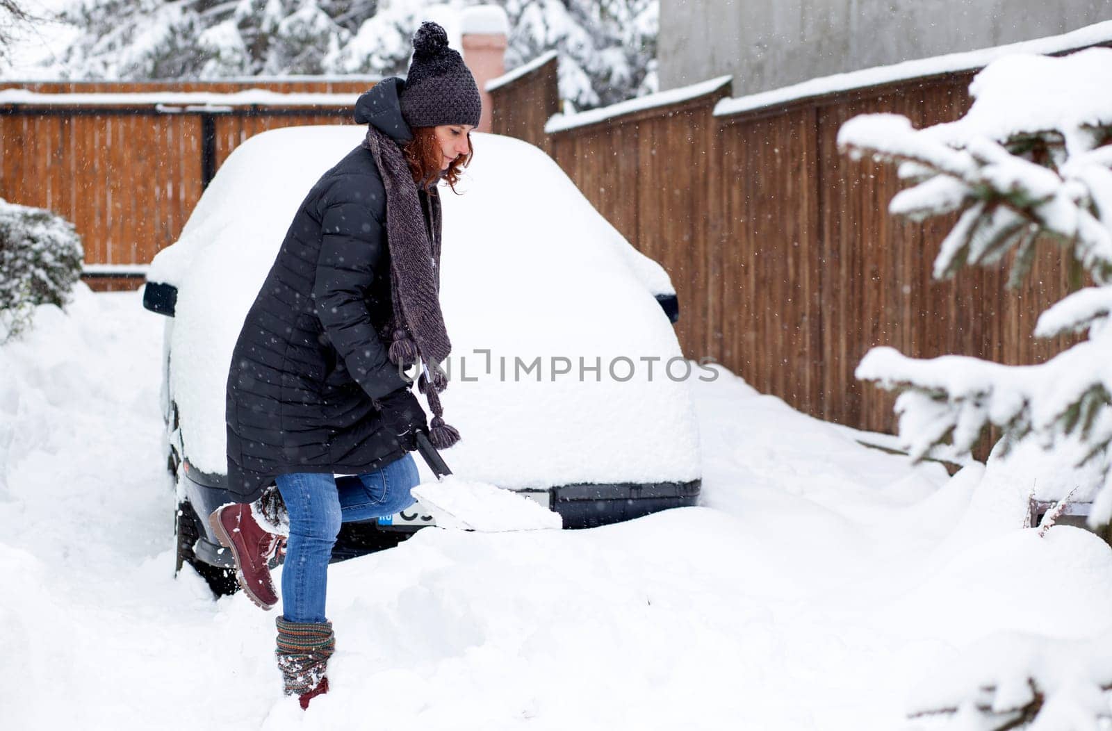 woman with shovel cleaning snow aeound car. Winter shoveling. Removing snow after blizzard