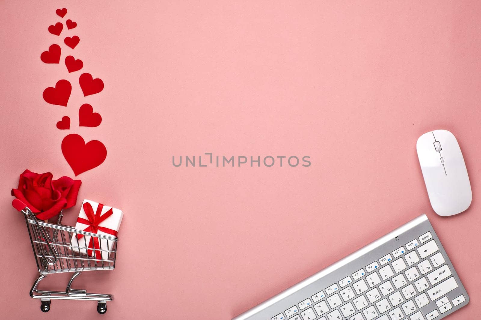 Shopping trolley, Computer keyboard and mouse, gift box, flower and decorative red hearts on pink background with copy space. Concept of internet shopping. Valentine's day, Mother's day, wedding