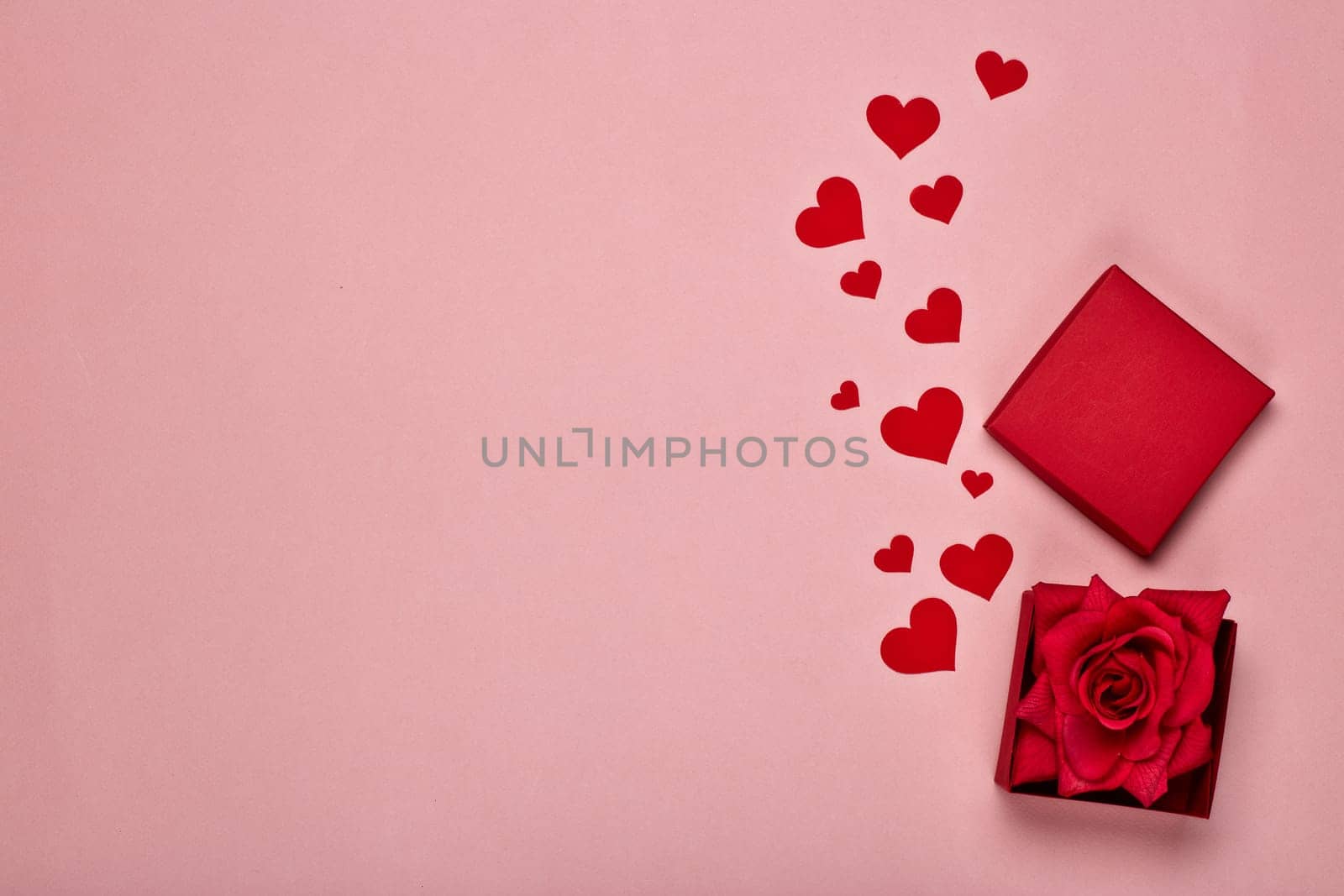 Red decorative hearts and gift box with rose on a pink background with copy space. Top view. Valentine's Day card. Design element for romantic greeting card, wedding invitation