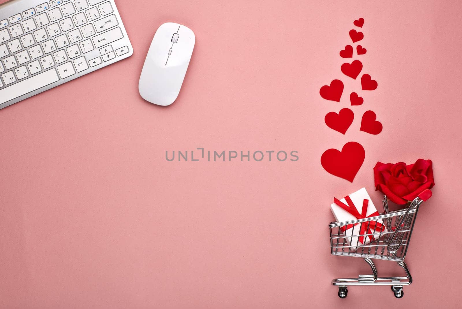 Shopping trolley, Computer keyboard and mouse, gift box, flower and decorative red hearts on pink background with copy space. Concept of internet shopping. Valentine's day, Mother's day, wedding