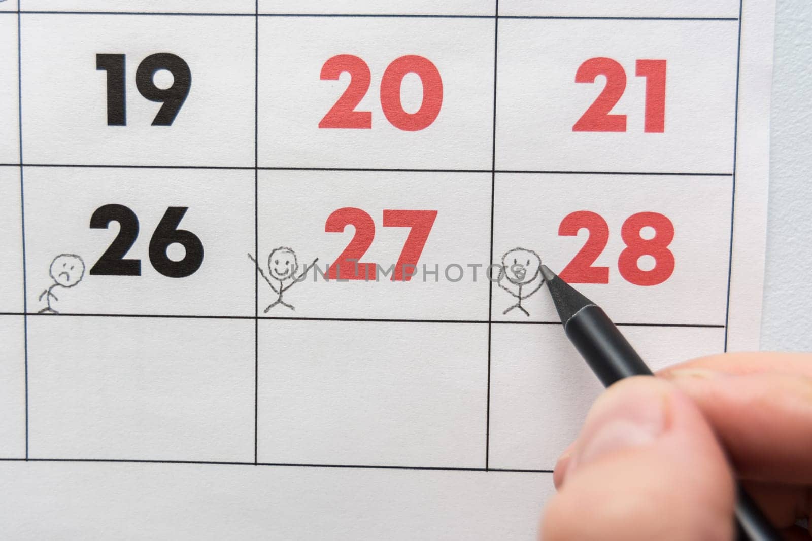 A pencil draws funny people on a sheet of a wall calendar