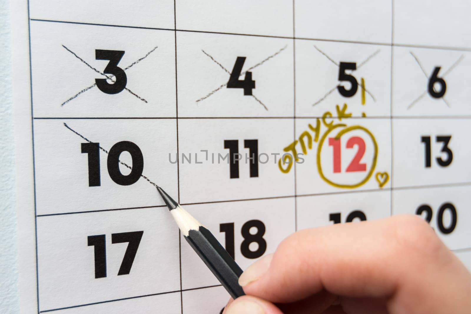 A hand crosses out the penultimate day before the holiday with a pencil in the calendar