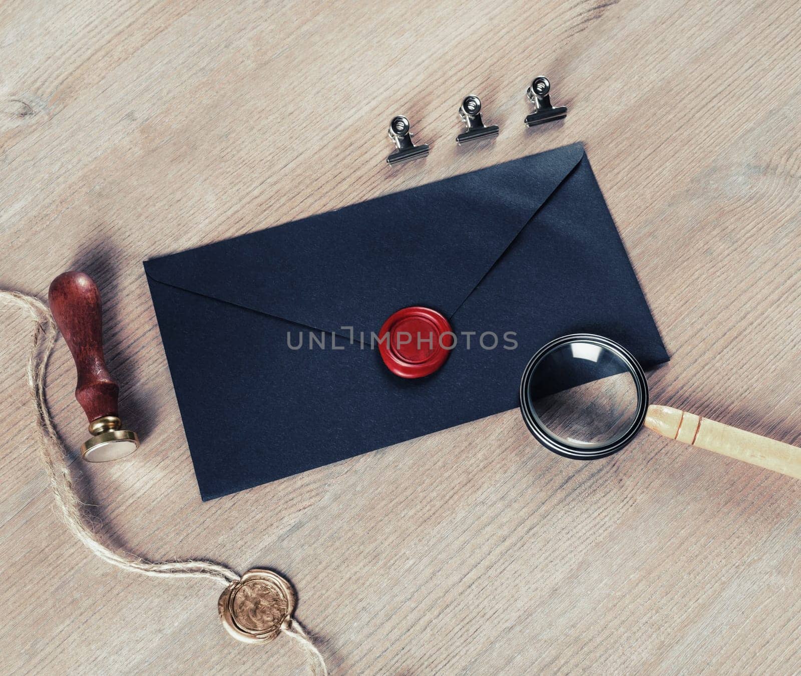 Old black envelope with red wax seal, magnifier and stamp on wooden background.