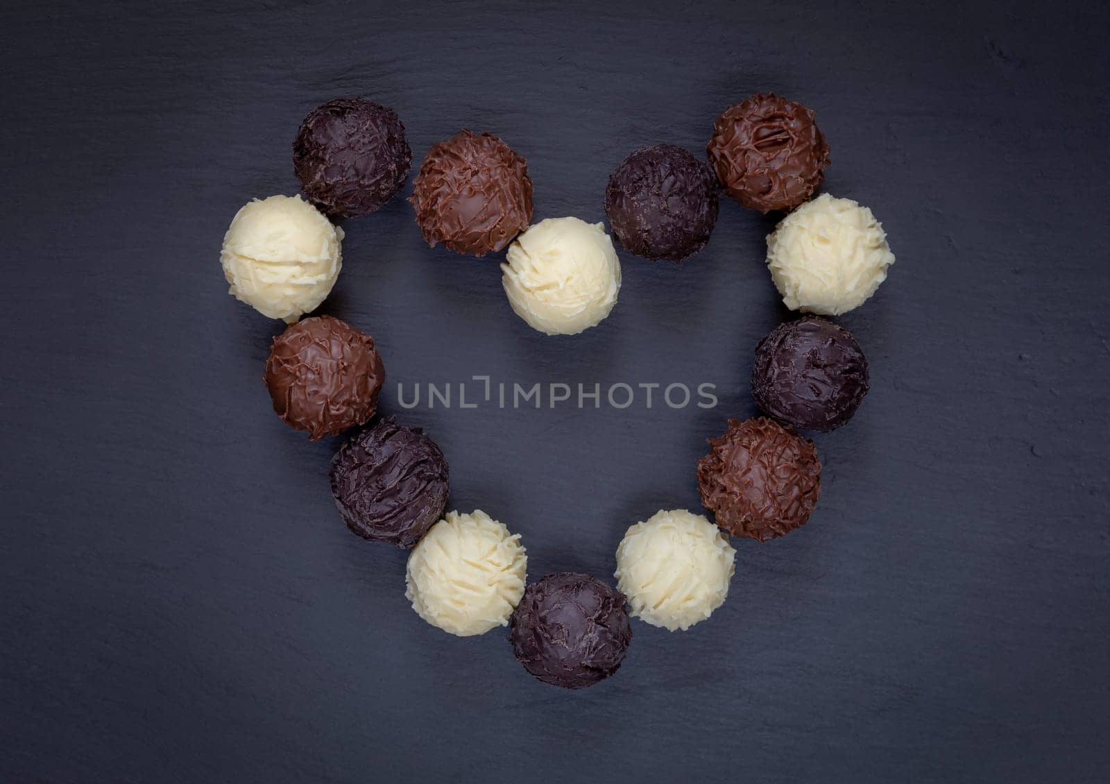 Chocolate truffles assortment heart shape on black stone.
