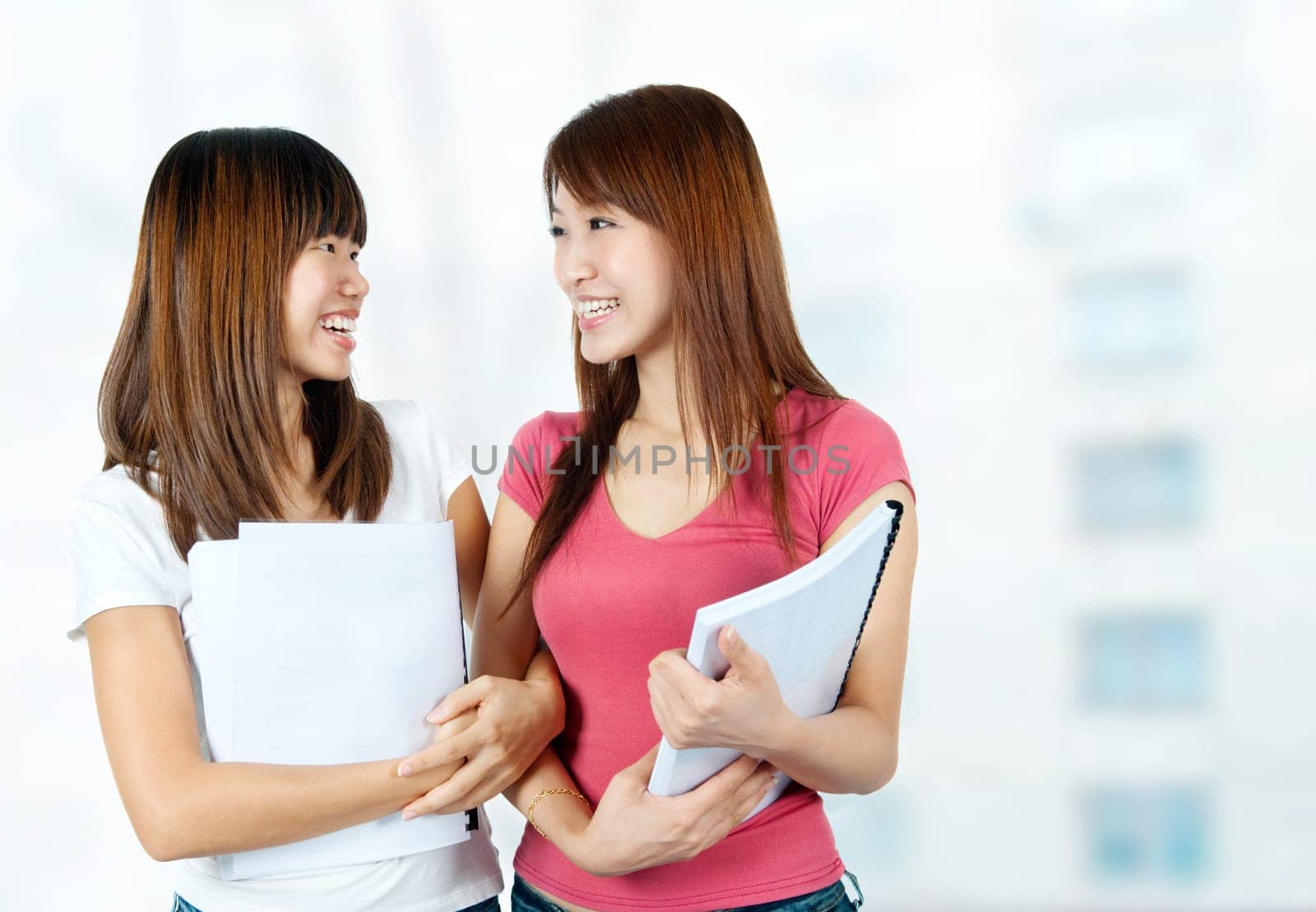 Two happy Asian students with books talking in school campus.