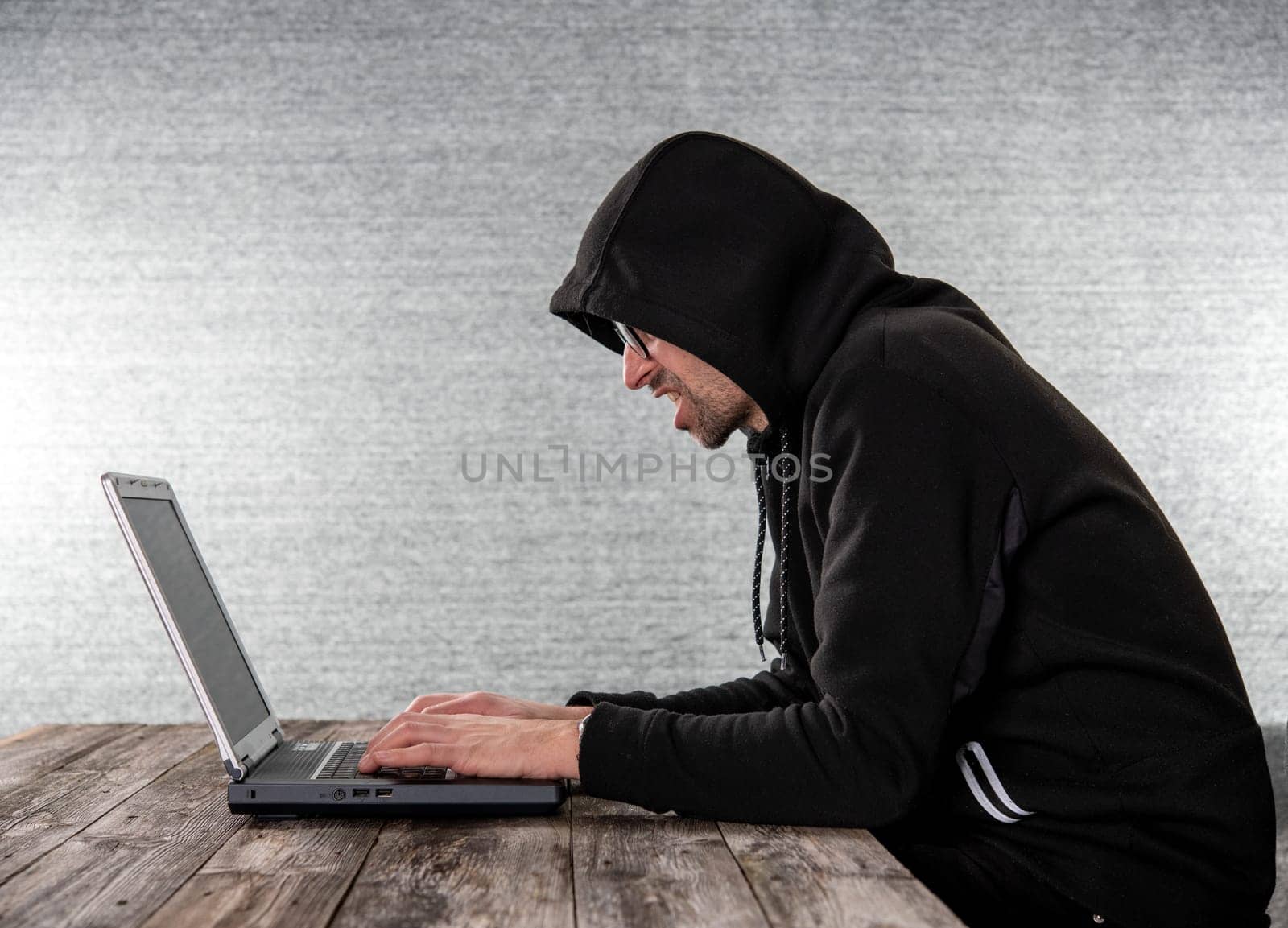 hacker in black hoody with laptop  in front of  gray background