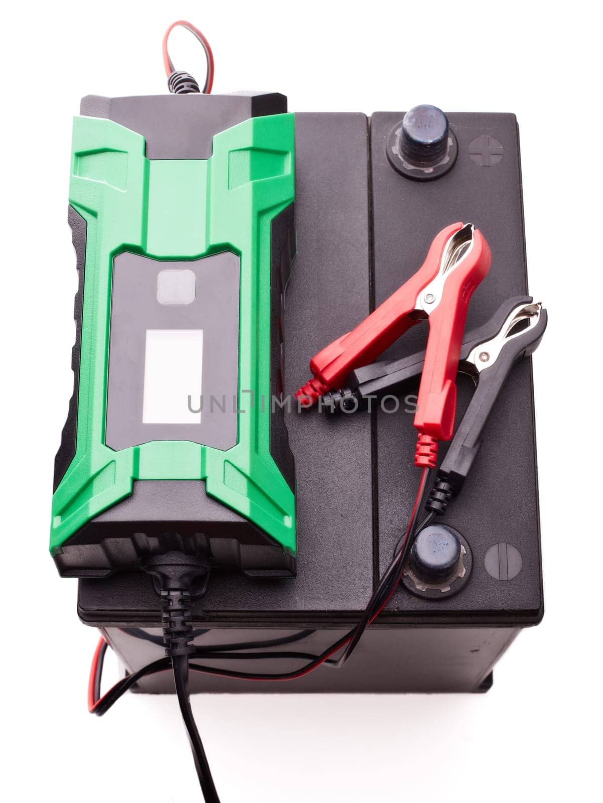 Black car accumulator battery and green charger isolated on a white background. Top view. Acid battery,12 volts supply. Concept of service, maintenance, charging car battery, diy